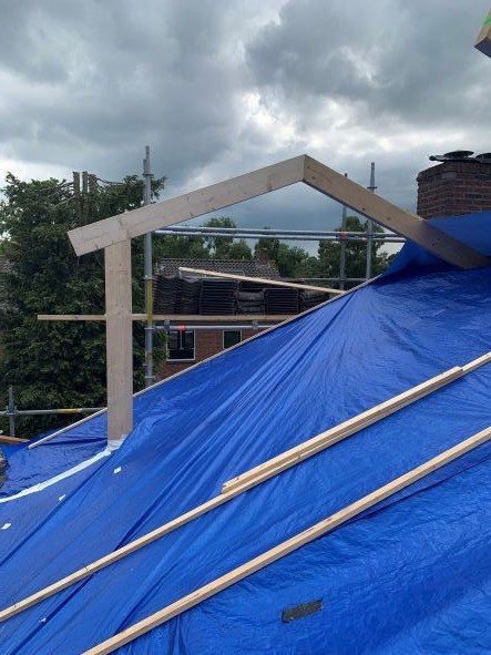 Nieuwe houten kapconstructie onder een blauw zeil tijdens een dakrenovatie
